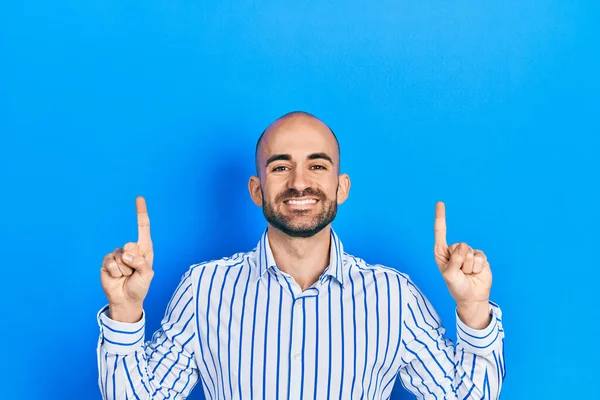 Young bald man pointing up with fingers smiling with a happy and cool smile on face. showing teeth.