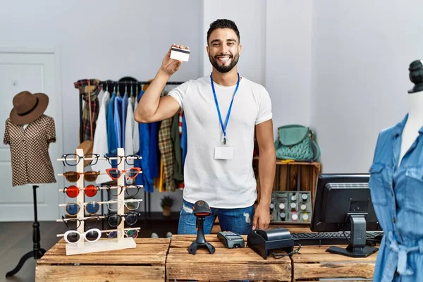 衣料品店で働いているクレジットカードを保持している若いアラブ人男性店主 — ストック写真