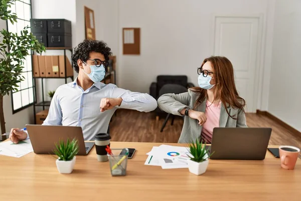 Two business workers wearing medical mask making elbow handshake at the office.