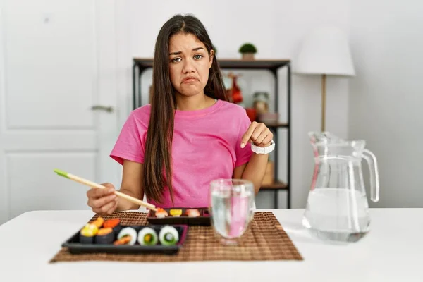 若いブルネットの女性は指で方向を示す 悲しいと動揺を指して箸を使用して寿司を食べる不幸なと落ち込んで — ストック写真
