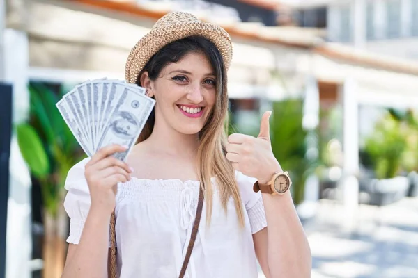Młoda Brunetka Trzyma Banknoty Dolarów Uśmiechnięte Szczęśliwy Pozytywny Kciuk Góry — Zdjęcie stockowe