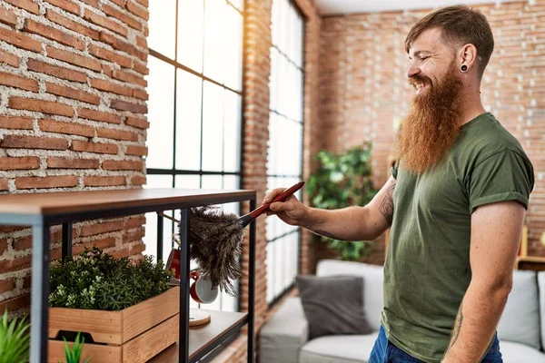Young redhead man smiling confident cleaning dust at home