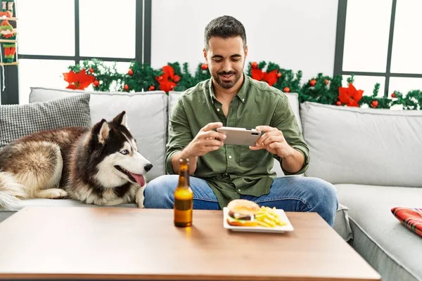 Young Hispanic Man Make Photo Hamburger Sitting Sofa Dog Christmas — Fotografia de Stock