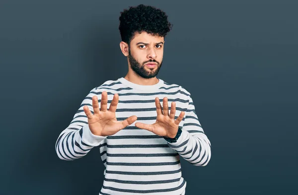 ひげを生やした若いアラブ人男性は 恐怖と嫌な表情で拒否と否定を示す手の手のひらを離れて移動カジュアルな縞模様のセーターを着ています 止めて禁止する — ストック写真