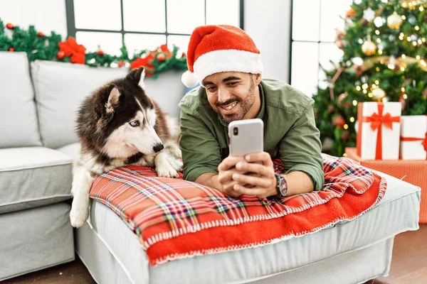 Young Hispanic Man Using Smartphone Lying Sofa Dog Christmas Tree — Photo