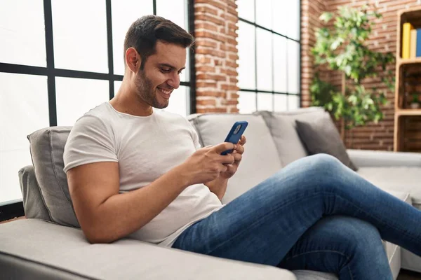 年轻的惊慌失措的男人坐在家里沙发上用智能手机 — 图库照片