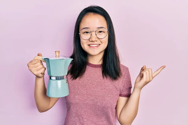 拿着意大利咖啡壶的年轻中国姑娘高兴地微笑着 手指手画脚地指向旁边 — 图库照片