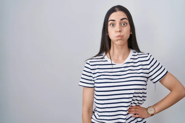 Young Brunette Woman Wearing Striped Shirt Puffing Cheeks Funny Face — Zdjęcie stockowe