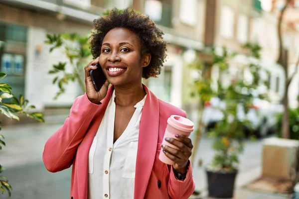 Beautiful business african american woman with afro hair smiling happy and confident outdoors at the city having a conversation speaking on the phone