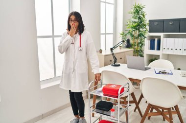 Doktor üniforması giyen genç İspanyol kadın ve steteskop ağızlarını eliyle kapatıyor, şok geçiriyor ve hata yapmaktan korkuyor. şaşırmış ifade 