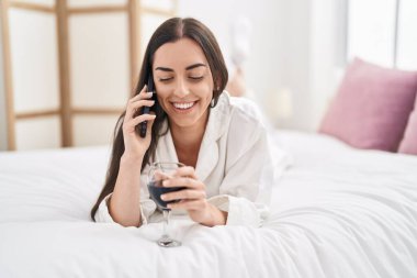 Genç İspanyol kadın akıllı telefonda konuşuyor. Yatak odasında şarap içiyor.