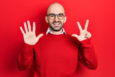 Genç kel adam, günlük kıyafetler ve gözlük takıyor. Sekiz numaralı parmaklarıyla gösteriyor ve işaret ediyor. Kendinden emin ve mutlu bir şekilde gülümsüyor.. 