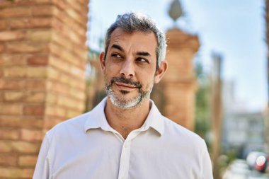 Orta yaşlı, kır saçlı, gülümseyen bir adam şehirde mutlu bir şekilde duruyor..