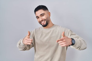 İzole edilmiş arka planda duran genç yakışıklı adam mutlu ve komik yüzüyle kamerayı işaret ediyor. İyi enerji ve titreşimler. 