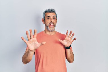 Gri tişörtlü yakışıklı orta yaşlı adam. Korkudan dehşete düşmüş ve korkmuş. El hareketlerini bırak, şok içinde bağır. panik konsepti. 