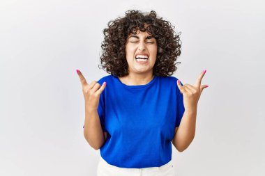 Ortadoğulu genç bir kadın izole edilmiş arka planda duruyor çılgın bir ifadeyle el kaldırarak rock sembolü yapıyor. Müzik yıldızı. ağır kavram. 