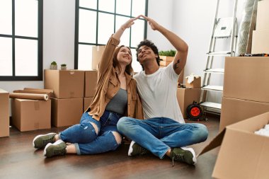 Mutlu bir şekilde gülümseyen genç çift yeni evlerinde elleri ile ev sembolü yapıyor..