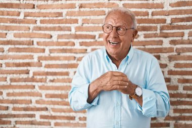 Tuğla duvarın üzerinde duran gri saçlı yaşlı adam. Gergin ve heyecanlı bir şekilde çenesine bakıp yan tarafa bakıyor. 