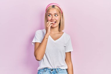 Gayri resmi beyaz tişört giyen güzel sarışın kadın gergin ve gergin görünüyor. Elleri ağızdan tırnak yiyor. anksiyete. 