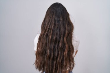 Young teenager girl standing over white background standing backwards looking away with crossed arms 