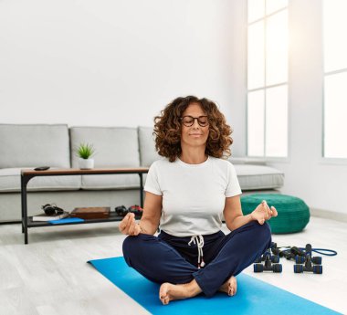 Olgun İspanyol kadın evdeki oturma odasında yoga meditasyonu yapıyor.