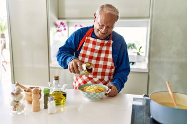 Son sınıf öğrencisi gülümsüyor. Mutfaktaki spagettiye domates sosu döküyor.