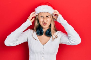 Güzel İspanyol kadın Noel şapkası takıyor ve kulaklık takıyor. Başı ağrıyor çünkü stres altında. migren ağrısı. 