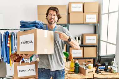 Gönüllü olarak hayır işi için bağış kutusu tutan yakışıklı orta yaşlı bir adam endişeli, endişeli ve şaşırmış bir ifadeye işaret ediyor. 