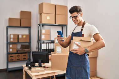 İspanyol asıllı genç bir iş adamı. Elinde paketler, ofisinde akıllı telefon kullanıyor.