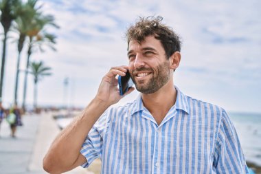 Genç İspanyol gülümseyen adam sahilde akıllı telefondan konuşarak mutlu oluyor.