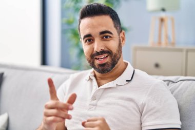 Kanepede oturan İspanyol genç adam evde konuşuyor.