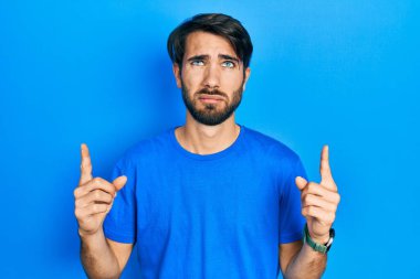 Gündelik kıyafetler giyen genç İspanyol adam üzgün ve üzgün görünüyor, parmaklarıyla yön gösteriyor, mutsuz ve depresif.. 