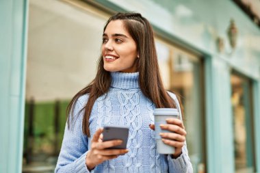 Genç İspanyol kız akıllı telefon kullanıyor ve şehirde kahve içiyor.