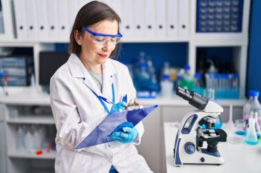 Orta yaşlı kadın bilim adamı gülümsüyor. Laboratuardaki panoda kendinden emin bir yazı var.