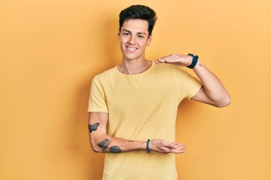 Sarı günlük tişörtler giyen, büyük ve büyük boylarda işaret eden İspanyol bir adam. Ölçü sembolü. Kameraya bakıp gülümsüyor. ölçüm kavramı. 