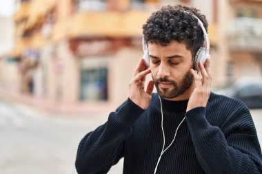 Genç Arap adam sokakta rahat bir ifadeyle müzik dinliyor.