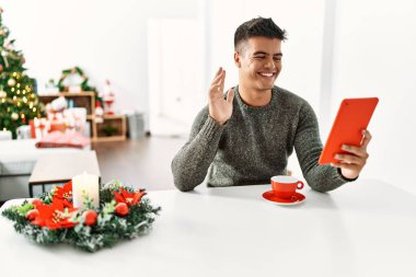 Evde Noel ağacının yanında oturan Latin asıllı genç bir adam var.