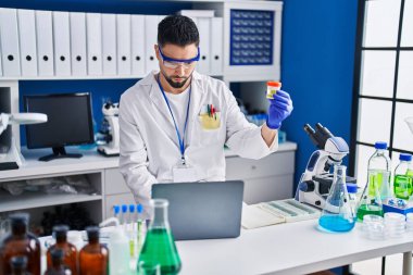 Genç Arap bilim adamı laboratuvarda idrar tüpü analizi yapmak için dizüstü bilgisayar kullanıyor.