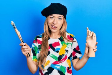 Kafkasyalı genç bir kadın sanatçı elinde küçük tahta manikin ve boya fırçaları tutarken hiçbir şeyden habersiz ve kafası karışık bir ifade sergiliyor. şüphe kavramı. 