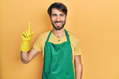 Daha temiz önlük ve eldivenler giyen genç İspanyol bir adam bir fikir veya soruyla gülümsüyor ve mutlu bir yüzle işaret ediyor. 