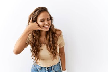 Güzel İspanyol kadın, arka planda tek başına durup gülümserken telefonla el ve parmaklarıyla telefonla konuşuyor gibi yapıyor. iletişim kavramları. 