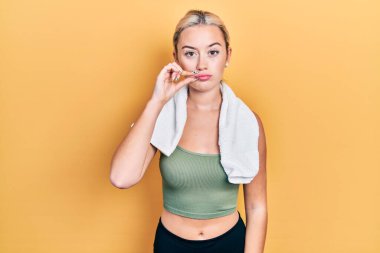 Spor kıyafetleri giyen, havlu ağızlı ve dudakları parmaklarıyla kapanan genç sarışın kız. gizli ve sessiz, tabu konuşması 