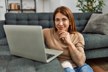 Orta yaşlı beyaz kadın akıllı telefon kullanıyor. Evde yerde oturuyor..