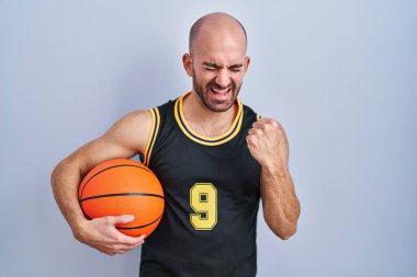 Sakallı, sakallı, basketbol forması giyen çok mutlu ve heyecanlı genç bir adam kolları havada, gülümseyen ve başarı için bağıran bir jest yapıyor. kutlama konsepti. 