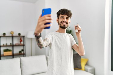 Genç İspanyol adam, elinde yeni evin anahtarı olan akıllı telefonun yanında selfie çekiyor.