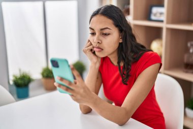 Genç Afro-Amerikalı kadın evde ciddi bir ifadeyle akıllı telefon kullanıyor.