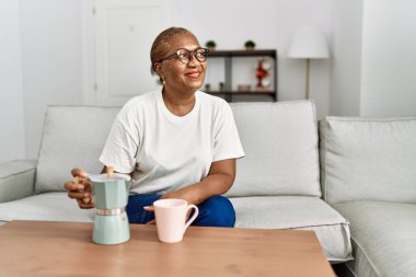 Kıdemli Afro-Amerikan kadın gülümseyerek evde kahve içiyor.