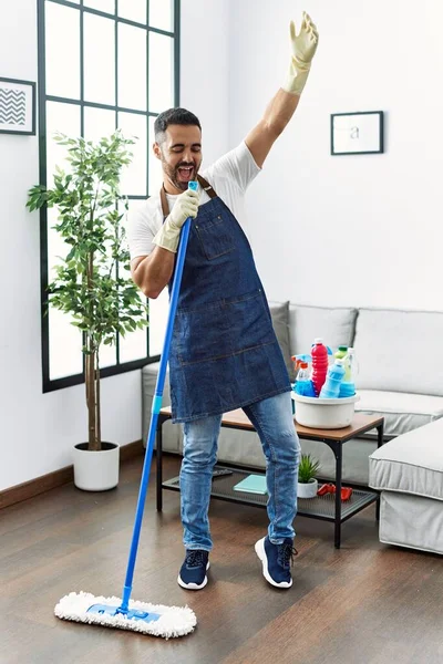 Young Hispanic Man Cleaning Floor Singing Song Using Mop Microphone — Stockfoto