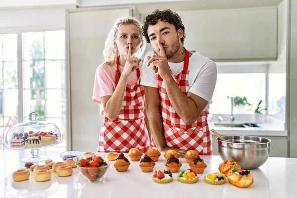 Couple of wife and husband cooking pastries at the kitchen asking to be quiet with finger on lips. silence and secret concept.