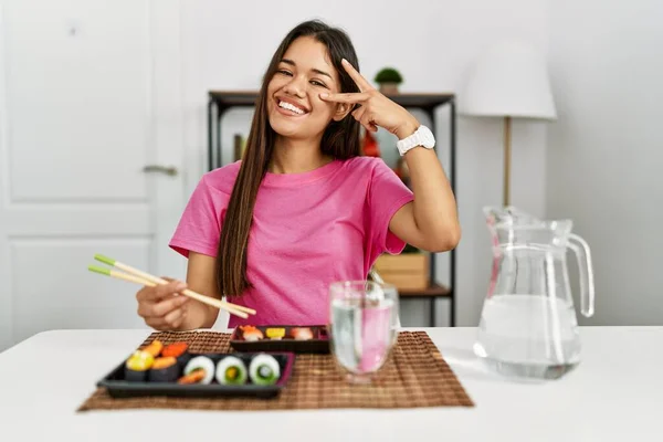 年轻的黑发女人用筷子吃寿司 用手指捂住脸做和平的象征 笑着表示胜利 — 图库照片